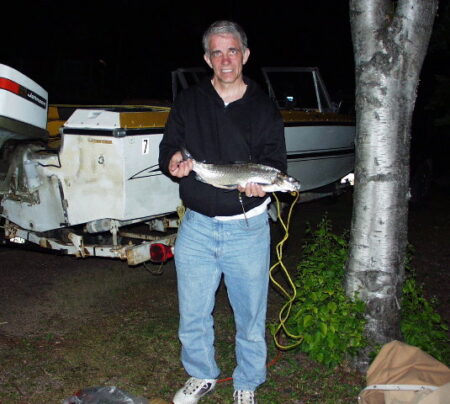 David Hall, posed in front of boat, holding fish in his hands.